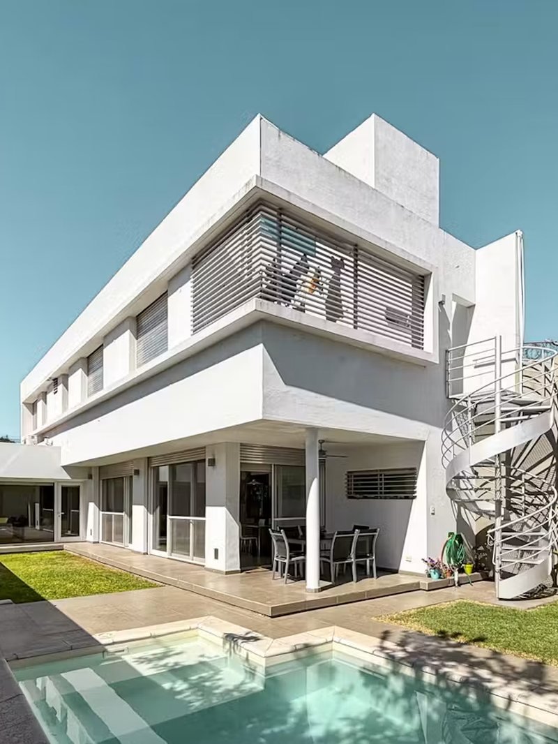 Frente de una casa moderna blanca con pileta y escalera caracol, de MG - Negocios Inmobiliarios