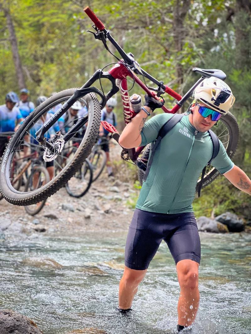 Ciclista de Seekers MTB cruzando un río con su bicicleta al hombro